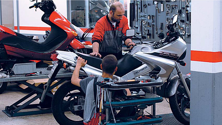 Garage automobile Photo d'un atelier où deux personnes travaillent sur une moto.